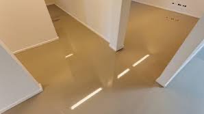 Beżowa, błyszcząca posadzka w pustym pomieszczeniu, widok z góry, z widocznymi promieniami słońca padającymi przez okno.