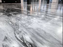 Błyszcząca, szara posadzka z efektem marmuru, odbijająca światło i elementy wystroju wnętrza, widoczne kolumny i fragment sufitu.