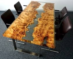 Stół z blatem z drewna o nieregularnym wzorze i żywicy epoksydowej imitującej rzekę, osadzony na metalowych nogach, otoczony krzesłami z ciemnej skóry.