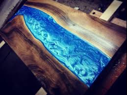 Blat stołu z drewna orzechowego z wypełnieniem z błękitnej żywicy epoksydowej imitującej rzekę z wirami i refleksami światła.