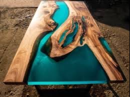 Stół z blatem z drewna orzechowego i wypełnieniem z turkusowej żywicy epoksydowej tworzącej wzór rzeki. Naturalne krawędzie drewna kontrastują z gładką powierzchnią żywicy.