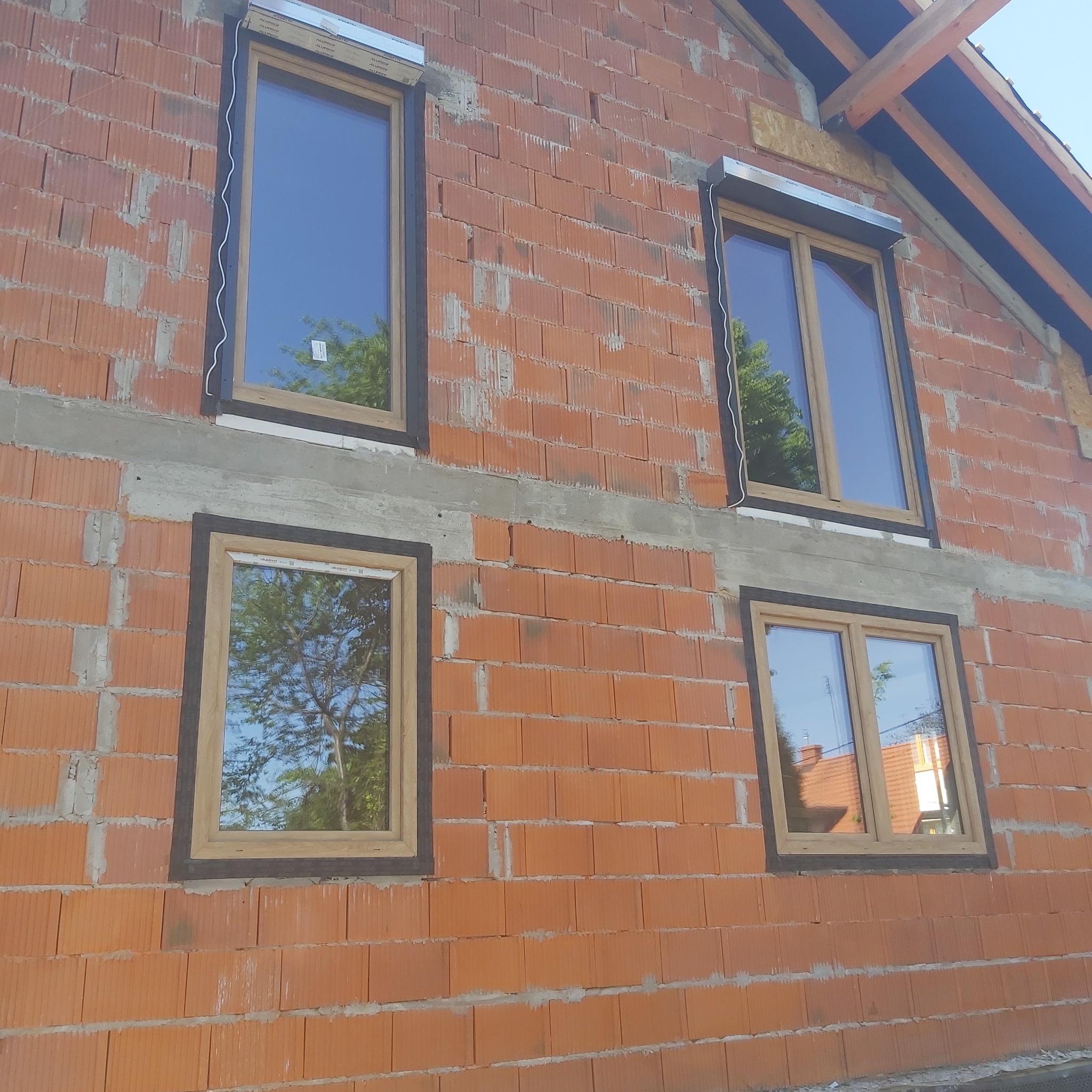 Surowy mur z czterema oknami z roletami zewnętrznymi w trakcie montażu, widoczne kable i niedokończona elewacja.