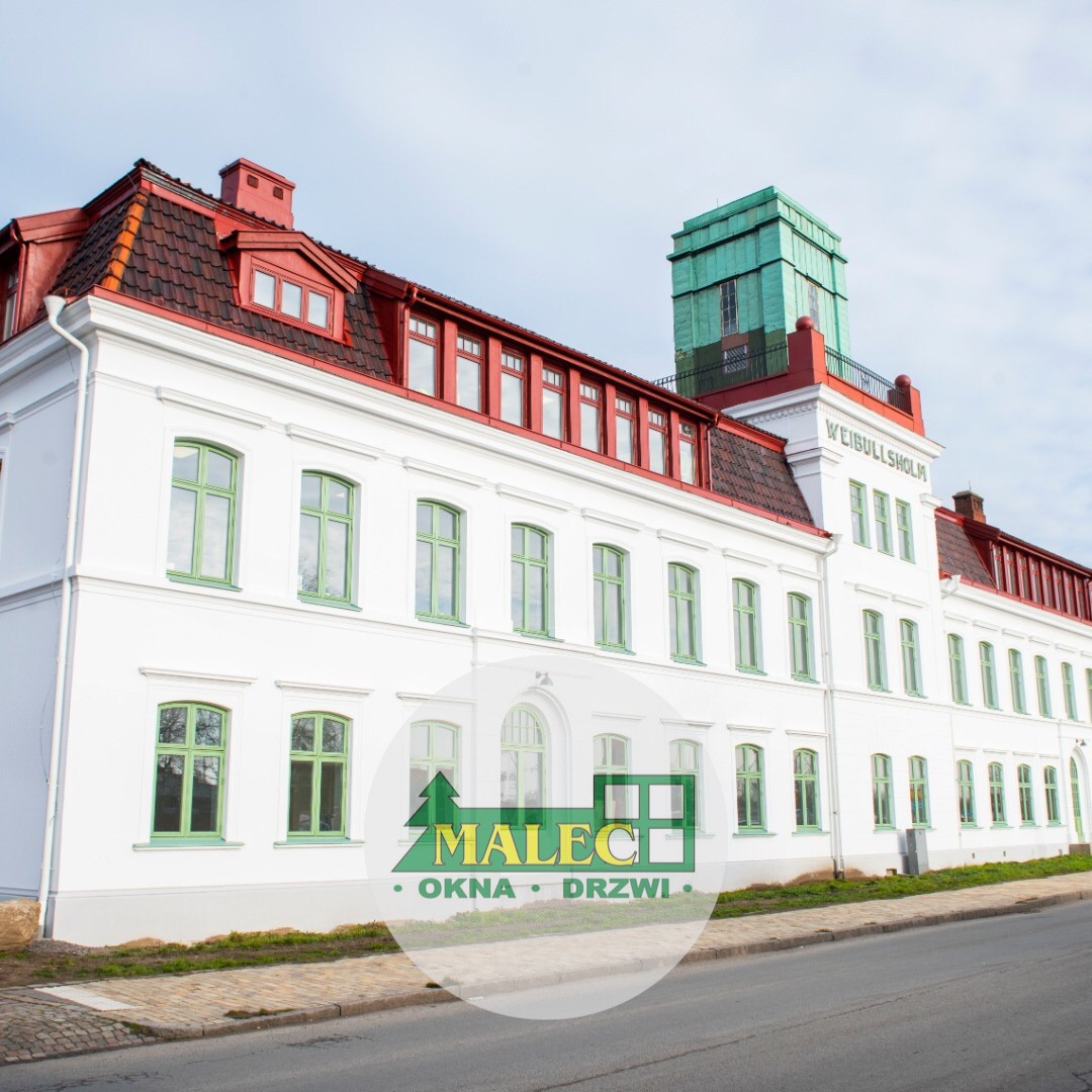 Biały budynek Weibullsholm z czerwonym dachem i zielonymi oknami, na pierwszym planie logo firmy z branży okien i drzwi.