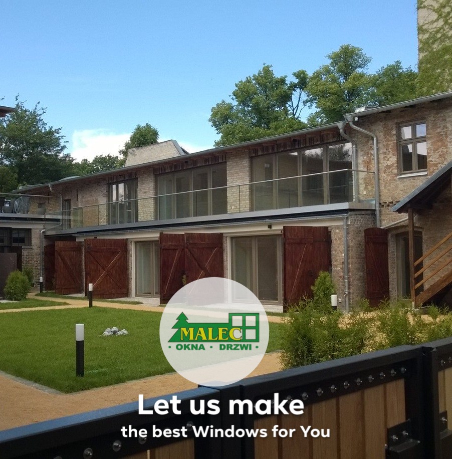 Budynek z drewnianymi okiennicami, balkonem z barierką i oknami, widok z poziomu trawnika, w tle logo firmy.