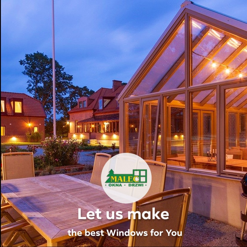 Szklana oranżeria przylegająca do domu z drewnianymi ramami okiennymi, widok z zewnątrz na drewniany stół i krzesła, w tle budynki w stylu szwedzkim oświetlone wieczorną porą, na pierwszym planie...