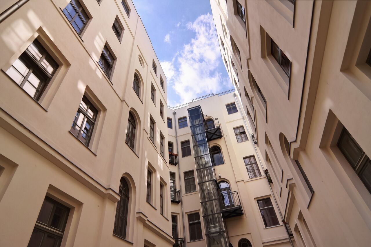 Wewnętrzny dziedziniec kamienicy z oknami i zewnętrzną windą, widok z dołu na błękitne niebo. Architektura miejska z perspektywy żabiej.