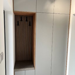 COMFORT ZONE - Szara szafa wnękowa z drewnianym wykończeniem, siedziskiem i wieszakami, oświetlona trzema reflektorami sufitowymi.