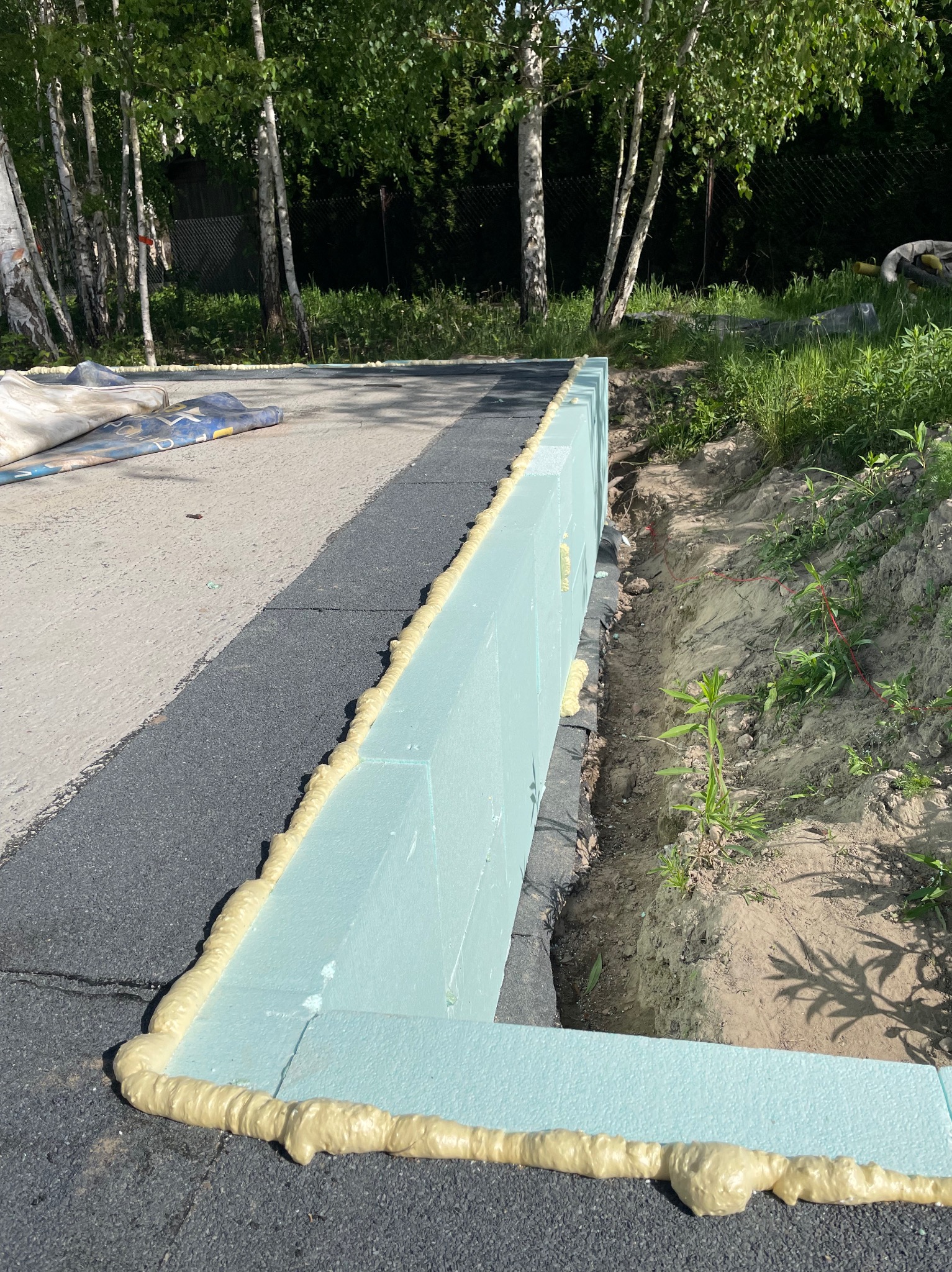 Budowa fundamentów: Ściana z niebieskich bloczków izolacyjnych, uszczelniona pianką montażową, w wykopie ziemnym, widok z góry.