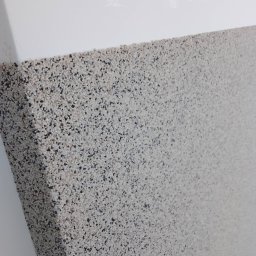 RENO-GŁADŹ MARCIN BRZOZOWSKI - Ściana z dekoracyjnym tynkiem mozaikowym w odcieniach szarości i bieli, kontrastująca z gładką, białą powierzchnią powyżej. Detal wykończenia wnętrza.