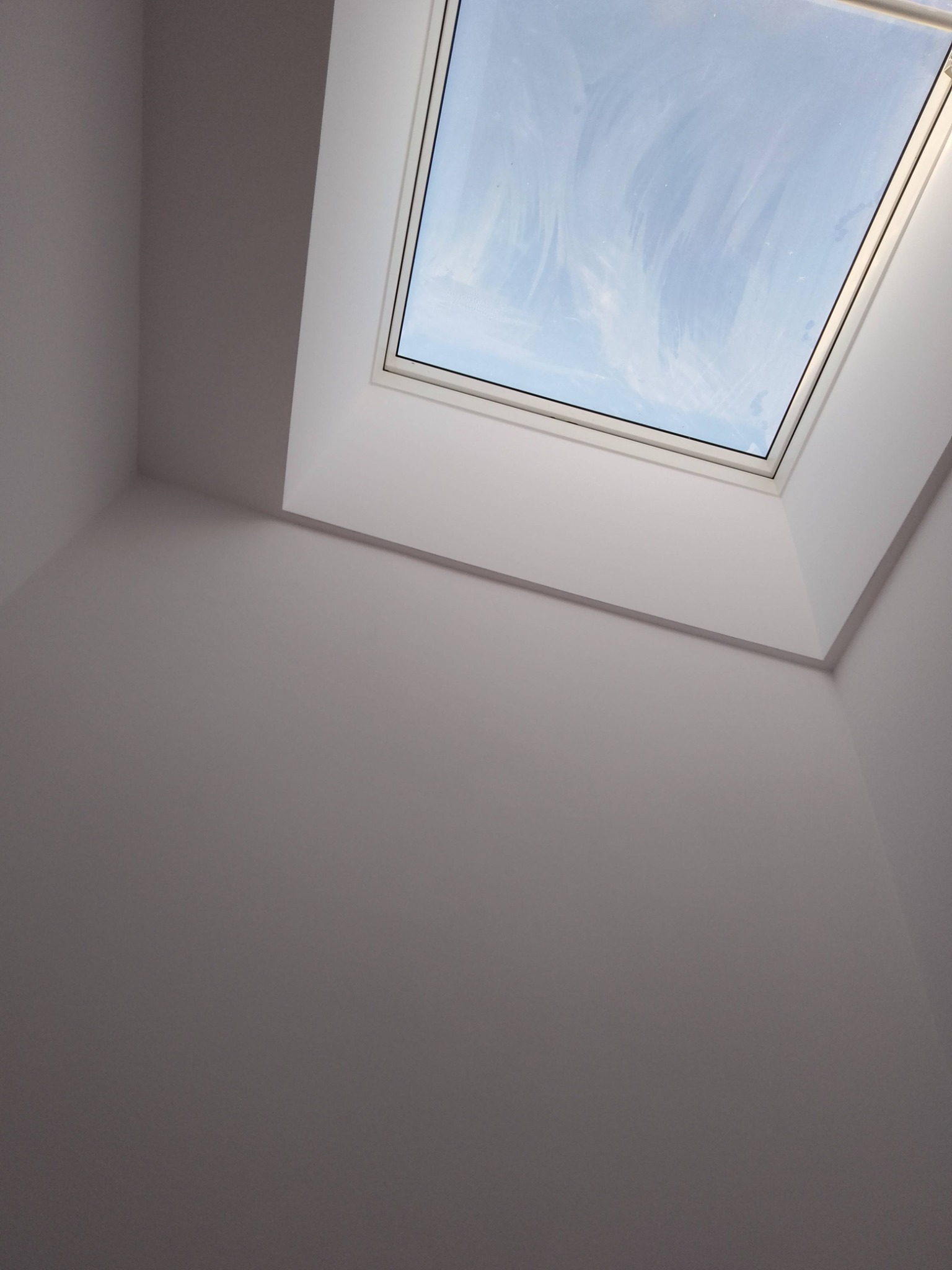 Wnętrze z oknem dachowym, świeżo pomalowane ściany w odcieniach bieli, widok na błękitne niebo przez okno. Minimalistyczny design, kątowe ujęcie.