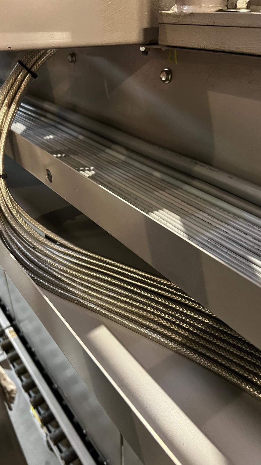 Metalowe rurki osłonowe kabli ułożone równolegle w metalowej konstrukcji, zabezpieczone czarnym zaciskiem.