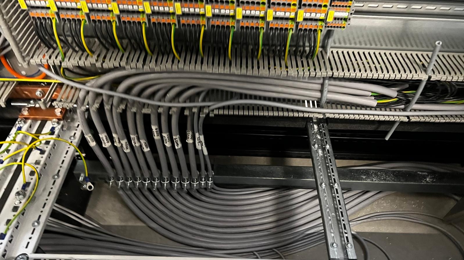 Panel sterowniczy z uporządkowanymi przewodami elektrycznymi, oznaczonymi etykietami, widoczne listwy zaciskowe i szyny montażowe.