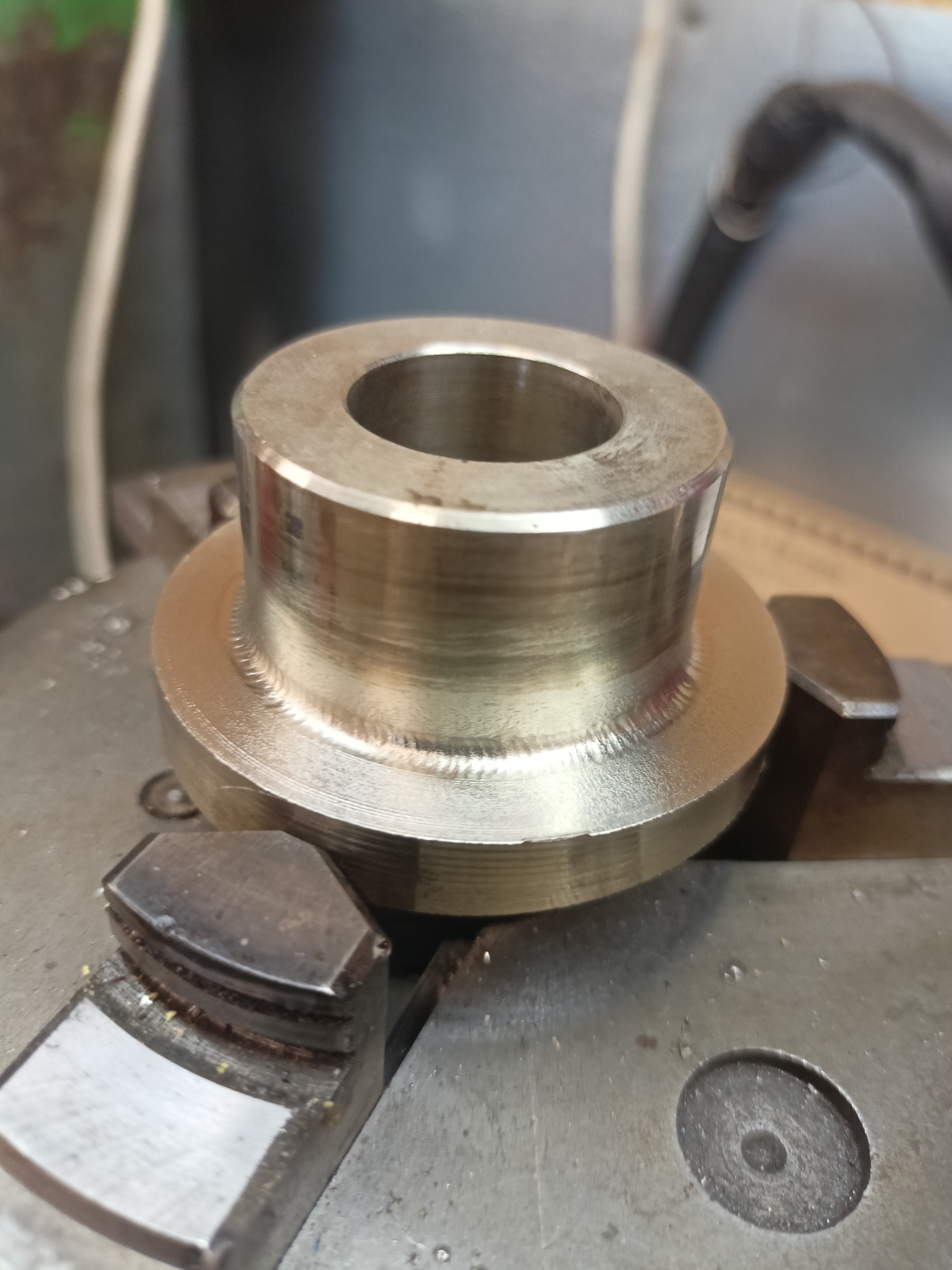 Metalowy element obrabiany na tokarce, widoczne ślady obróbki skrawaniem i uchwyt tokarski.