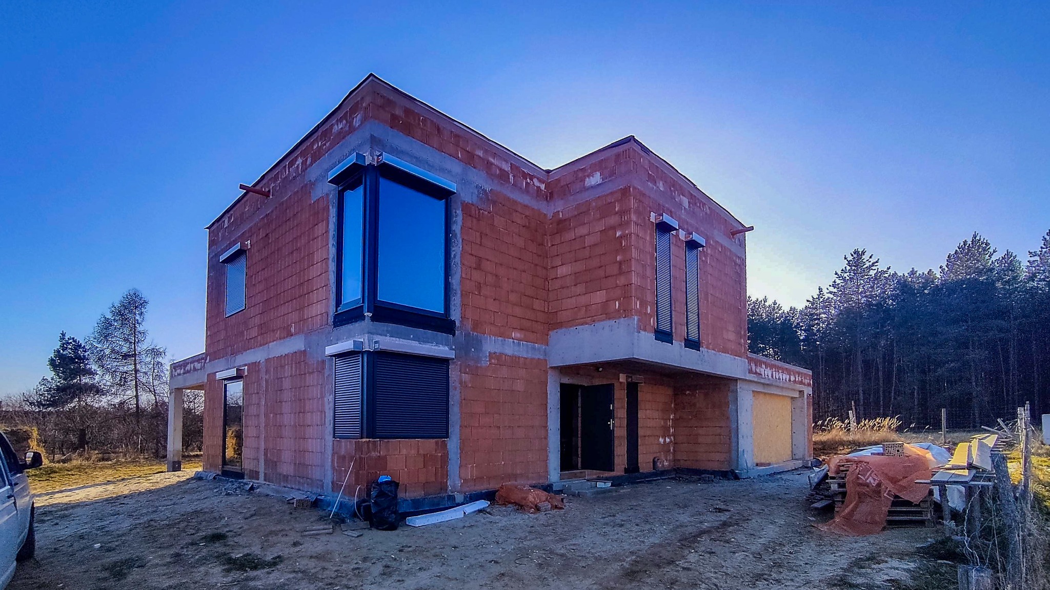 Dom w stanie surowym otwartym w Łańce z zamontowanymi oknami z czarnymi ramami i opuszczonymi roletami zewnętrznymi w kolorze grafitowym.