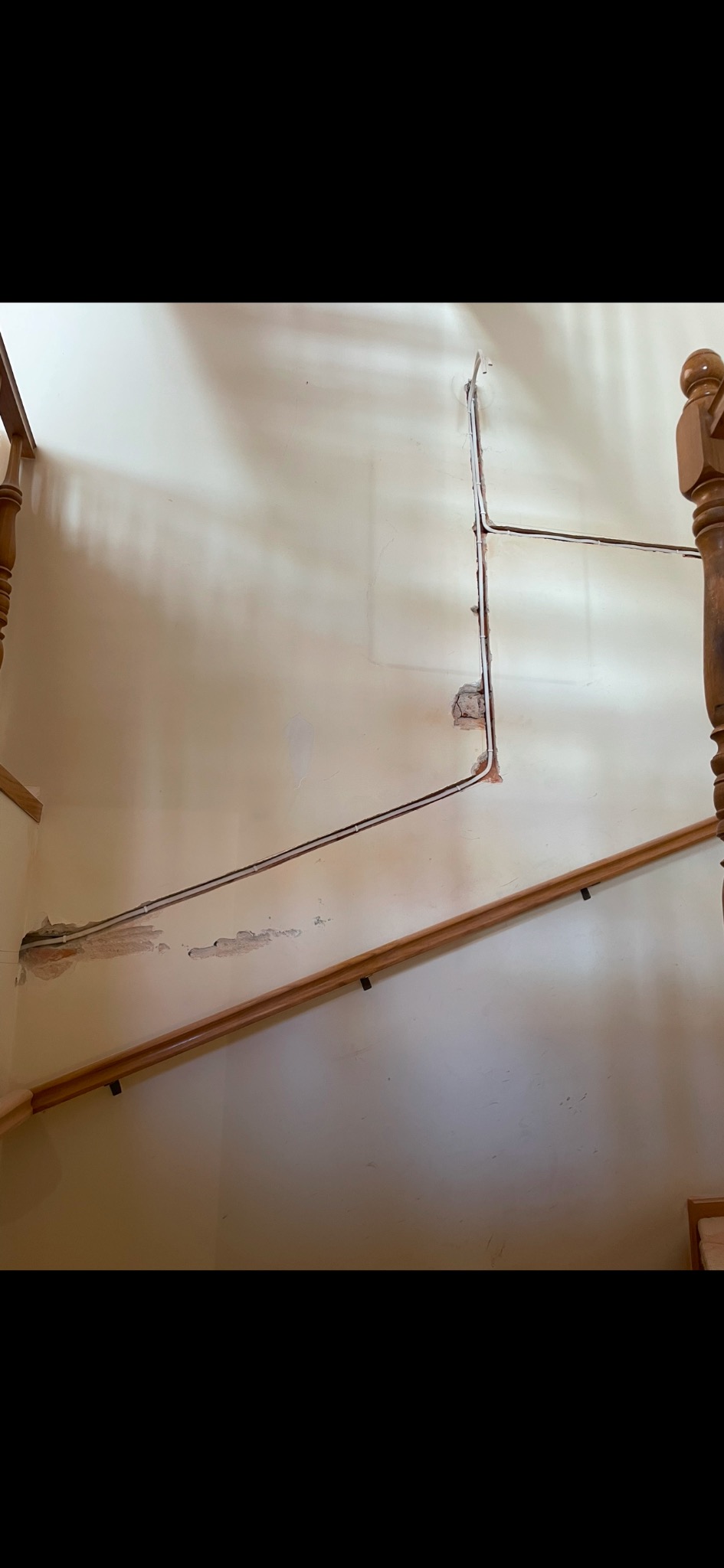 Ściana klatki schodowej z odkrytymi przewodami elektrycznymi i uszkodzeniami tynku wokół nich.