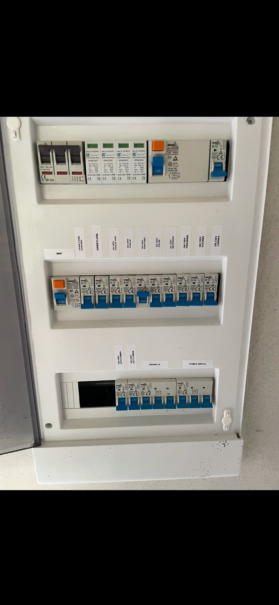 Rozdzielnica elektryczna z bezpiecznikami automatycznymi, opisana etykietami 'WRP', 'Oświetlenie dzwonek', 'Oświetlenie', 'GN 230V pokoje', 'GN 230V korytarz', 'GN 230V korytarz', 'GN 230V salon'...