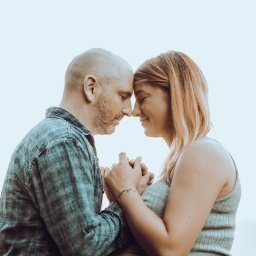 FQ Fotografia - Czułe ujęcie profilu kobiety w ciąży i mężczyzny, trzymających się za ręce, z czołami delikatnie dotykającymi się na tle jasnego nieba.