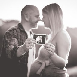 FQ Fotografia - Przyszli rodzice trzymający zdjęcie USG na tle zachodzącego słońca, ciepłe odcienie sepii i delikatne rozmycie tła.