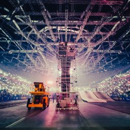 FQ Fotografia - Wnętrze hali widowiskowej z konstrukcją sceny, rampą i wózkiem widłowym na tle widowni oświetlonej telefonami komórkowymi.