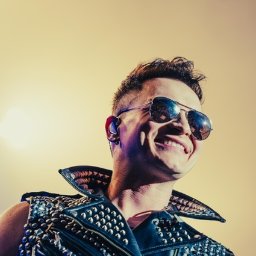 FQ Fotografia - Uśmiechnięty mężczyzna w skórzanej kamizelce nabijanej ćwiekami i okularach przeciwsłonecznych typu pilot, widok z dołu, oświetlenie sceniczne.