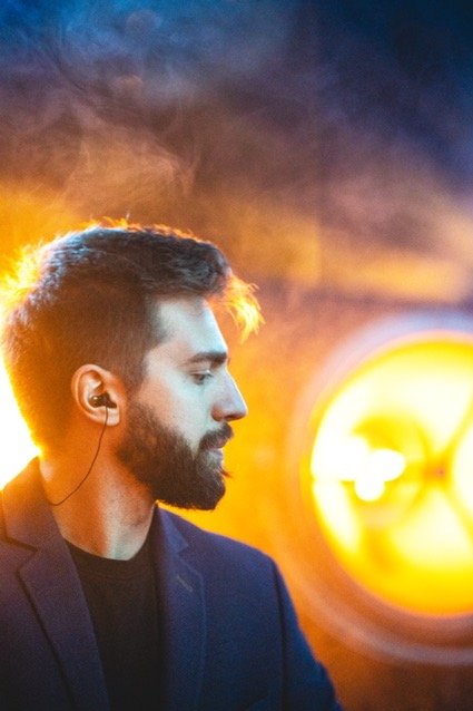 Mężczyzna z brodą w profilu, w słuchawkach, oświetlony pomarańczowym światłem z efektem dymu.