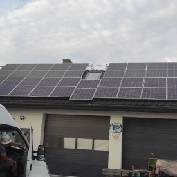 Alpha Pover - Instalacja paneli słonecznych na dachu budynku gospodarczego z bramą garażową; widoczny biały samochód dostawczy i monter w środku.