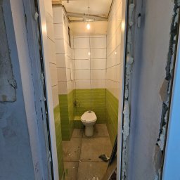 Viet-Pol - Wnętrze remontowanej łazienki z biało-zielonymi płytkami, widok przez niedokończone futryny drzwiowe z pianką montażową, sufit w trakcie prac wykończeniowych.