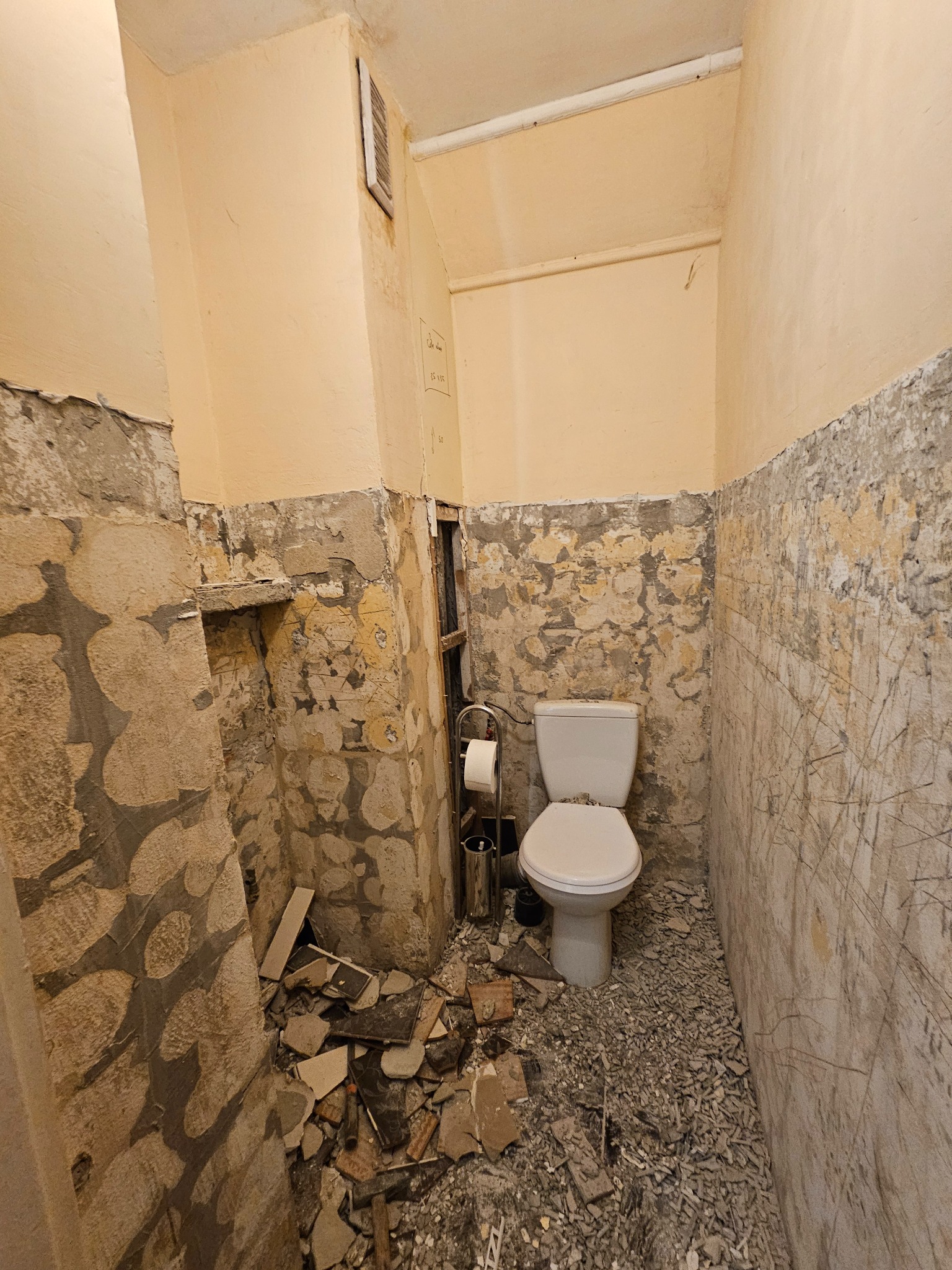 Łazienka w trakcie demontażu płytek i przygotowania ścian do dalszych prac, widoczne pozostałości po skuciu, surowe ściany i toaleta.