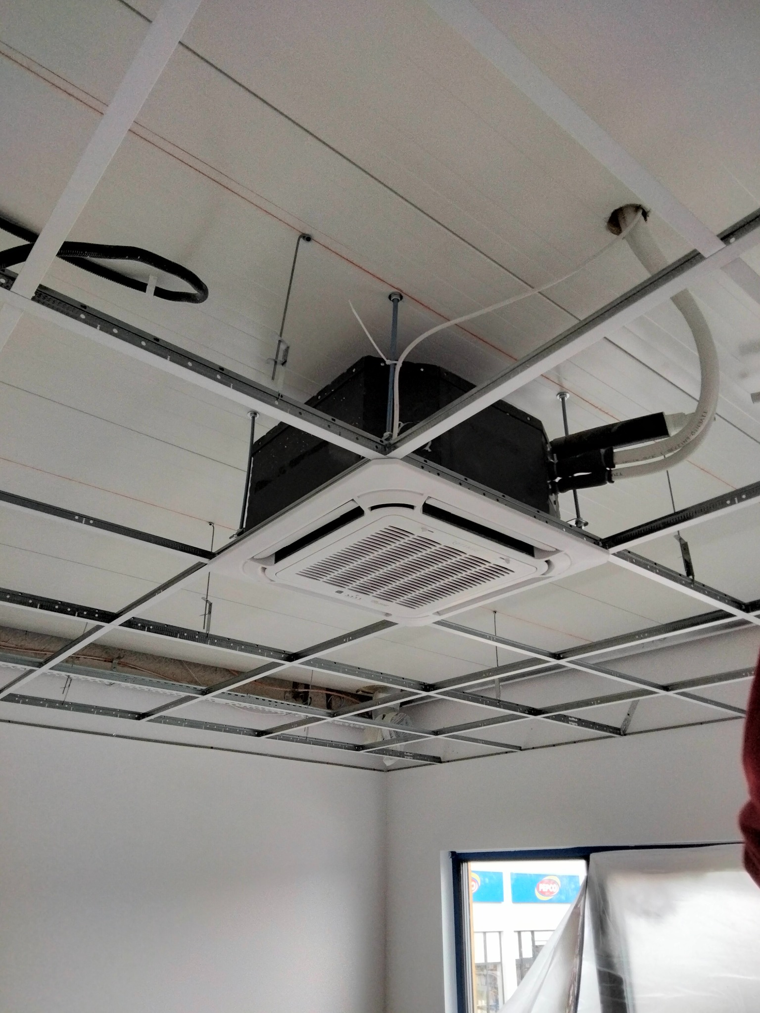 Kasetonowa jednostka klimatyzacji sufitowej zamontowana w pomieszczeniu biurowym, widoczne elementy konstrukcji podwieszanego sufitu, rury i przewody instalacyjne