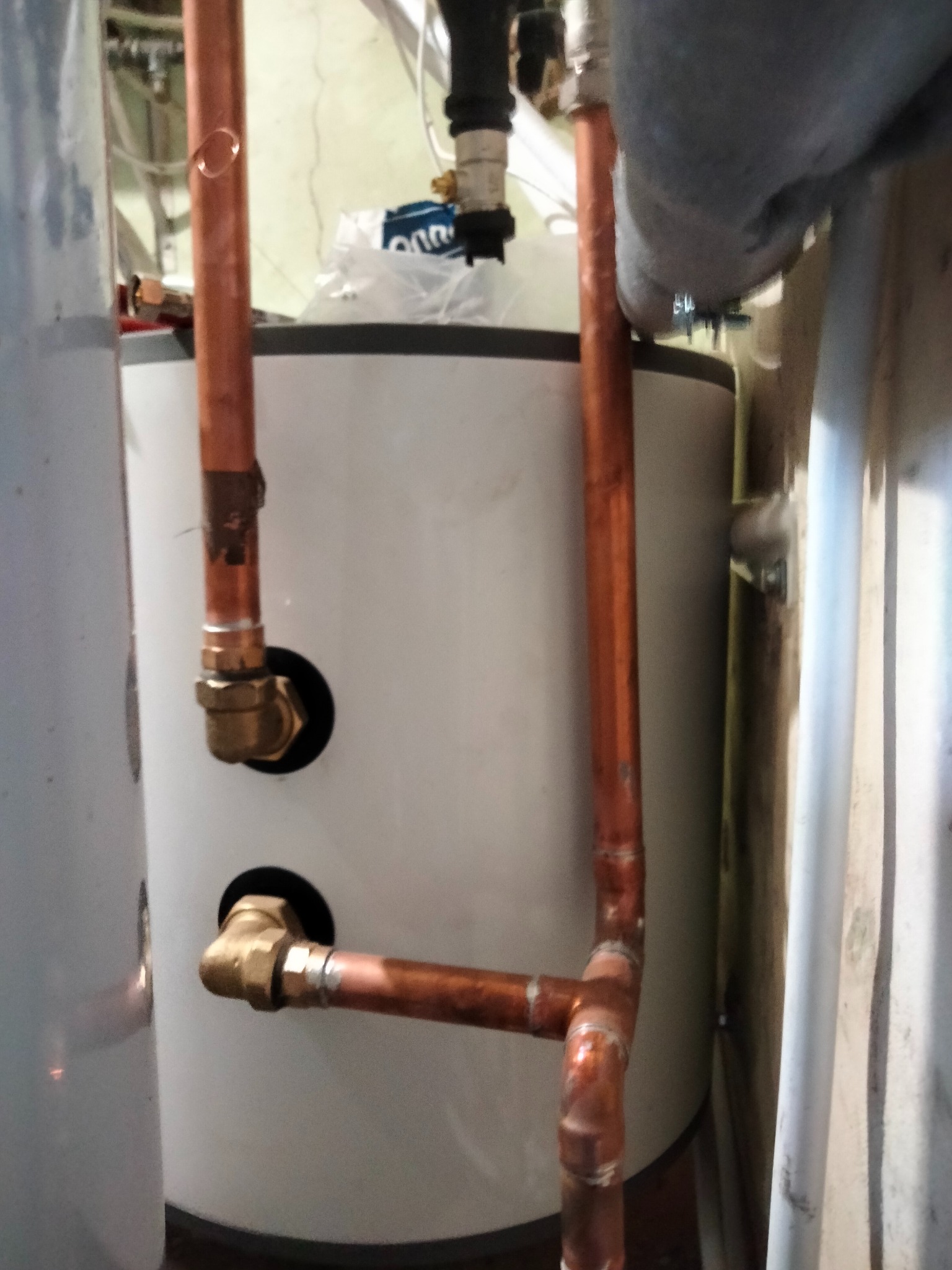 Montaż instalacji hydraulicznej do bojlera: miedziane rury połączone z zaworami, widoczne ślady lutowania na rurach, instalacja w trakcie podłączania.