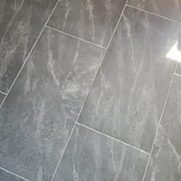 Szare płytki podłogowe imitujące marmur, ułożone ukośnie, widoczne fugi i odbicie światła.