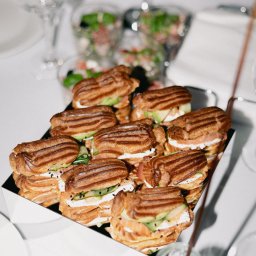 SS GASTRO SPÓŁKA Z OGRANICZONĄ ODPOWIEDZIALNOŚCIĄ - Eklery z łososiem, awokado i ogórkiem na czarnej tacy, część zastawy stołowej w tle. Elegancki catering na przyjęcie.