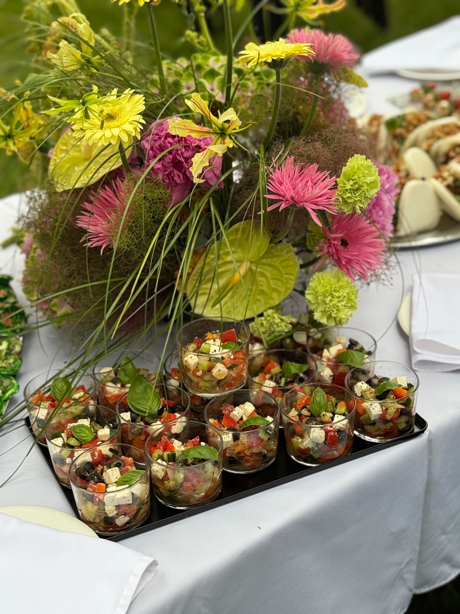 Dekoracyjne szklanki z sałatką caprese na tacy, z kwiatową dekoracją w tle, gotowe do serwowania w Warszawie. Elegancki catering.