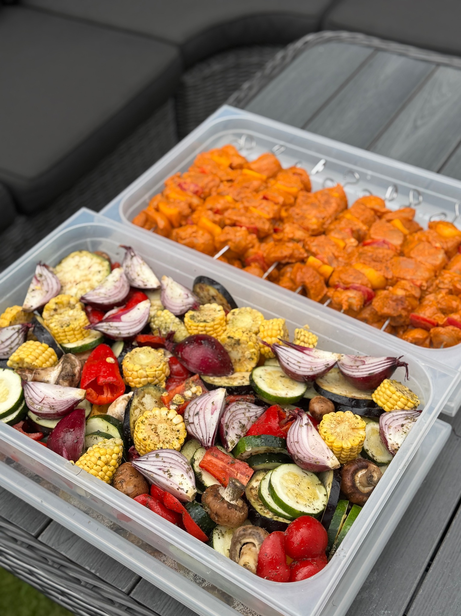 Dwa pojemniki z przygotowanymi warzywami i szaszłykami, gotowymi do grillowania. Kolorowe warzywa i mięso na szpadkach, idealne na letnie przyjęcie.