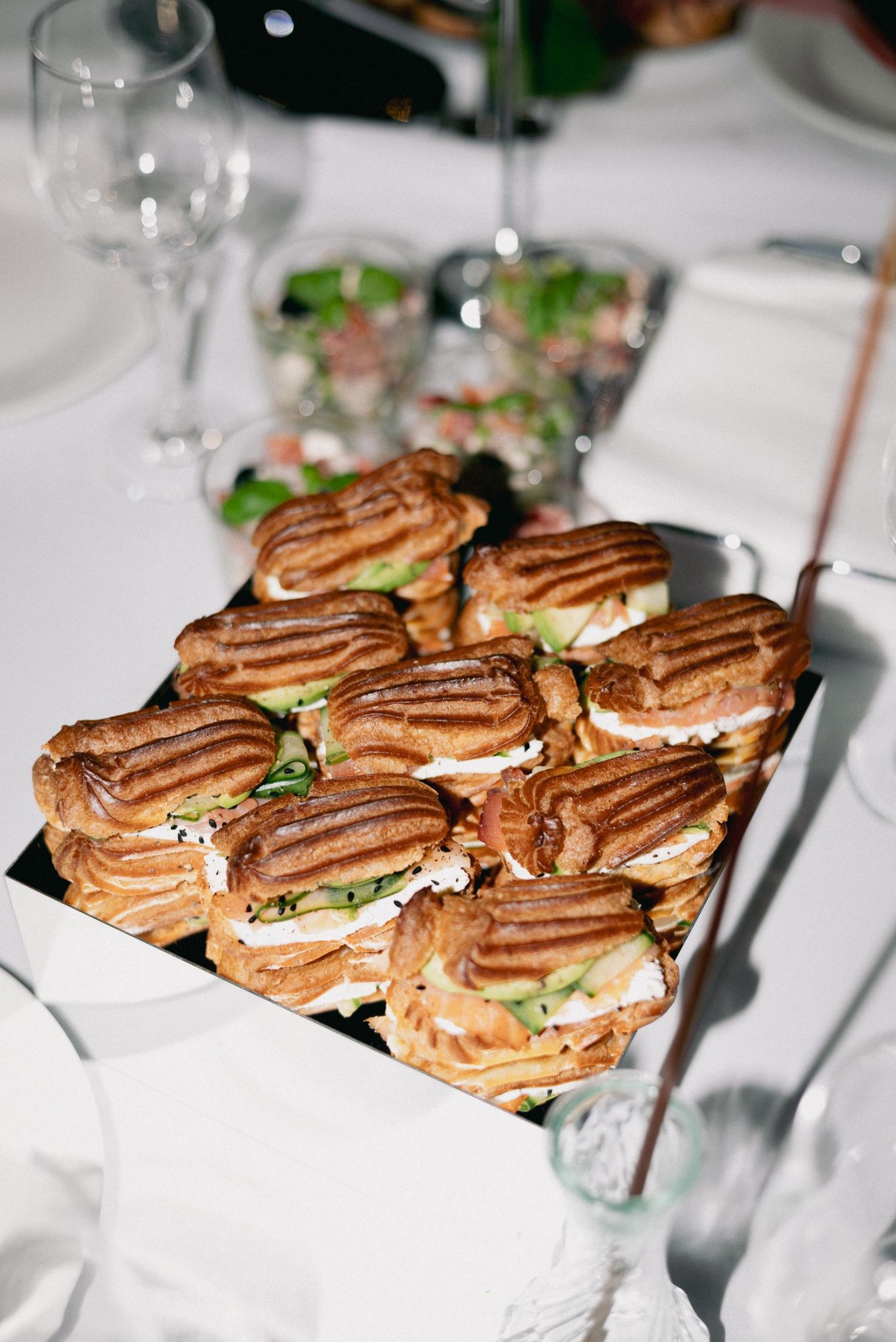 Eklery z łososiem, awokado i ogórkiem na czarnej tacy, część zastawy stołowej w tle. Elegancki catering na przyjęcie.