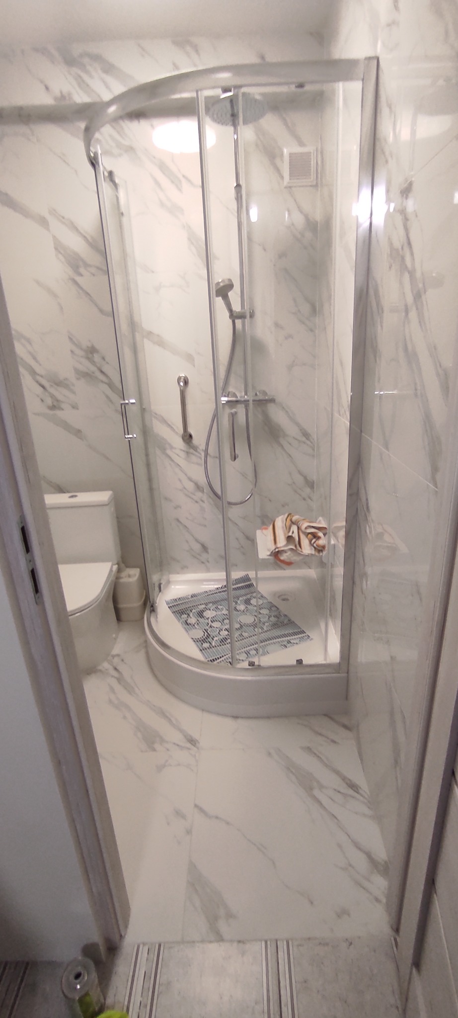 Nowoczesna kabina prysznicowa z hydromasażem w łazience wykończonej marmurowymi płytkami. Widoczna toaleta i fragment wejścia.