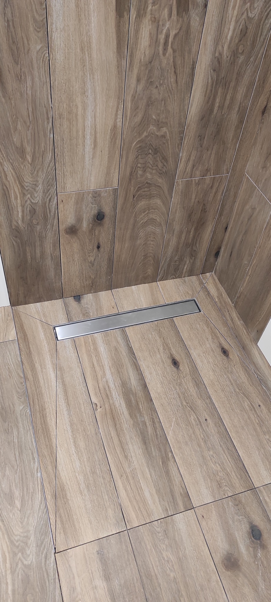 Wykończona kabina prysznicowa z odpływem liniowym i płytkami imitującymi drewno na ścianach i podłodze. Ułożenie płytek w pionie.