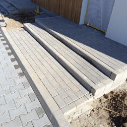 Firma usługowo-budowlana NIKITA Paulina Walczyńska - Schody wejściowe z szarej kostki brukowej prowadzące do budynku z drewnianą elewacją, widoczne niedokończone prace ziemne wokół schodów.