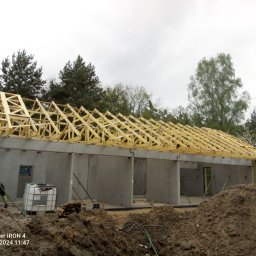 MAR-BUD - Konstrukcja drewniana dachu na surowym budynku z betonu komórkowego, widoczne ocieplenie na ścianie bocznej, w tle drzewa.