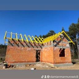 MAR-BUD - Wznoszenie murów z czerwonej cegły i montaż żółtej konstrukcji więźby dachowej na budowie domu jednorodzinnego w słoneczny dzień.