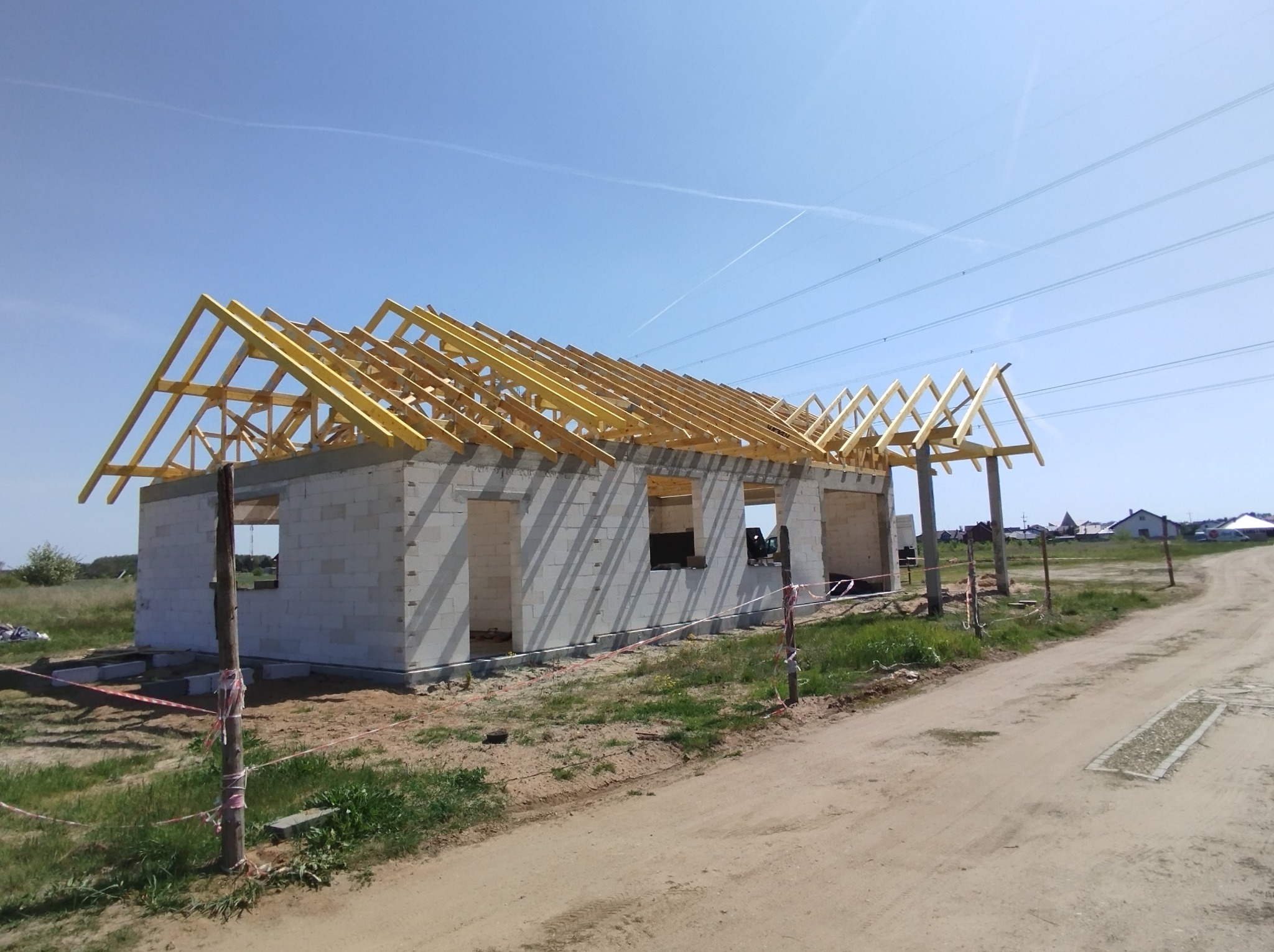 Wznoszenie konstrukcji drewnianej dachu na surowym budynku z betonu komórkowego, widok z zewnątrz w słoneczny dzień.