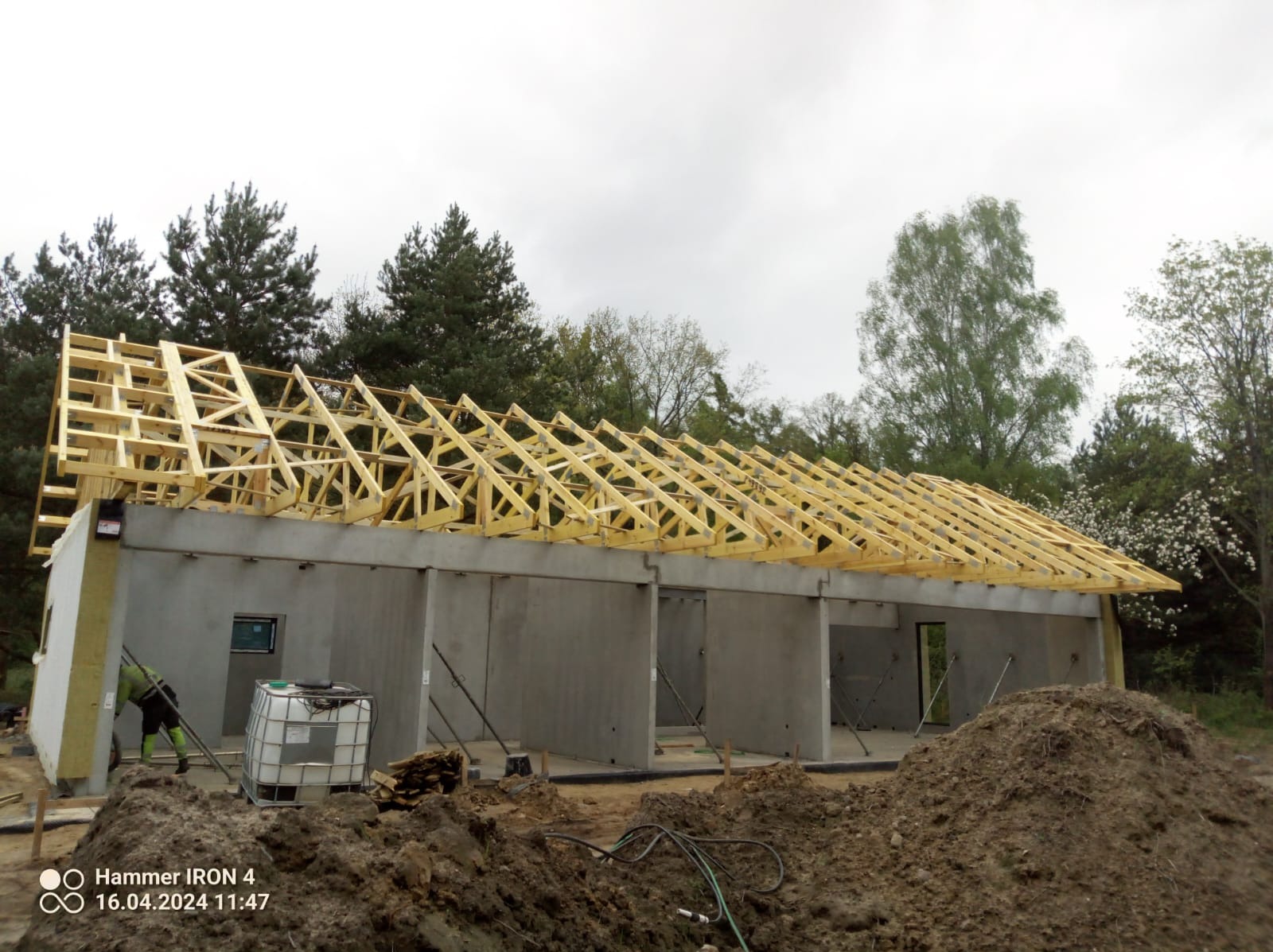 Konstrukcja drewniana dachu na surowym budynku z betonu komórkowego, widoczne ocieplenie na ścianie bocznej, w tle drzewa.