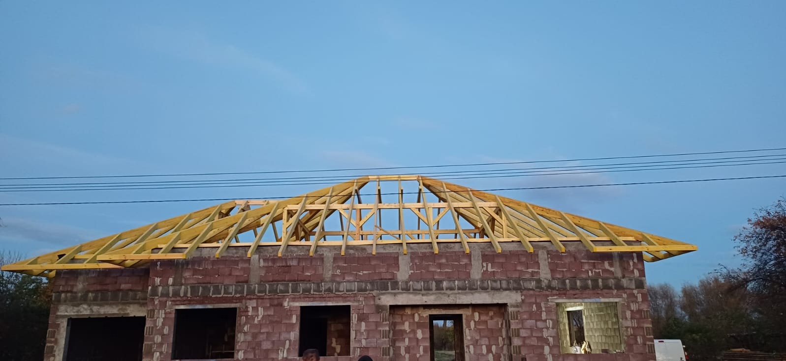 Surowy budynek z czerwonej cegły z drewnianą konstrukcją dachu w trakcie budowy, widok z dołu, błękitne niebo w tle.