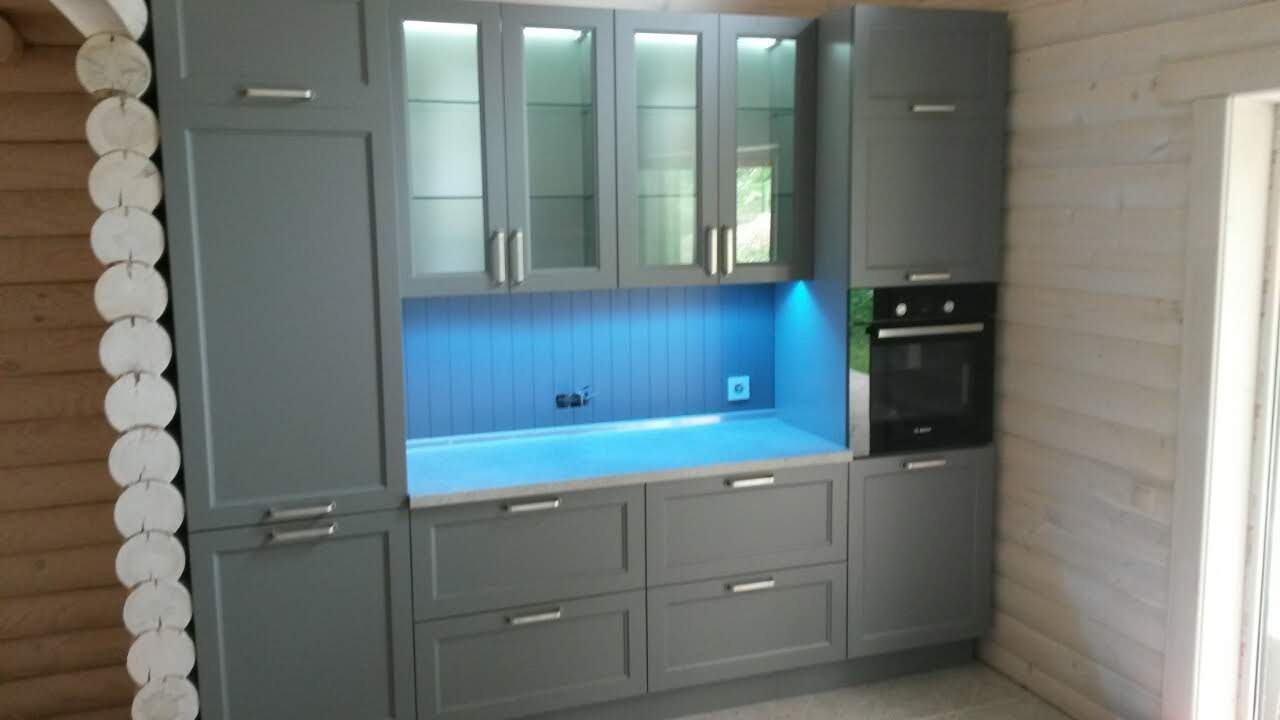 Szara zabudowa kuchenna w domu z bali, z podświetleniem LED i szklanymi frontami szafek wiszących.