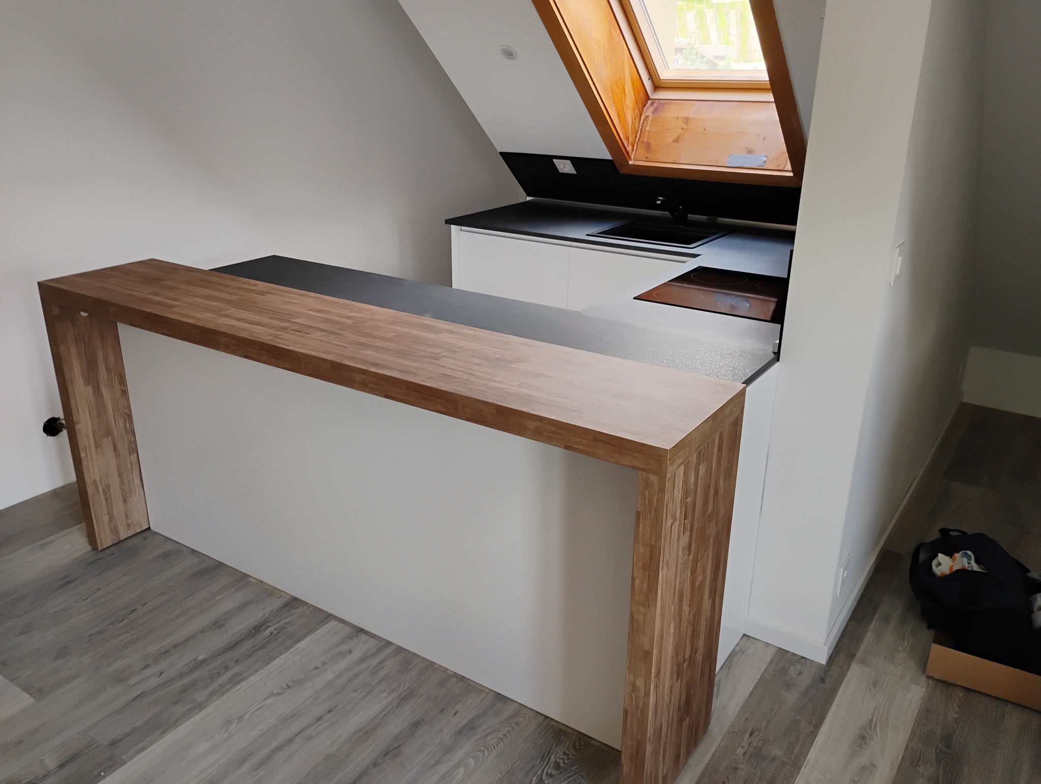 Nowoczesna kuchnia na poddaszu ze skośnym oknem dachowym, drewnianym blatem i białą zabudową.