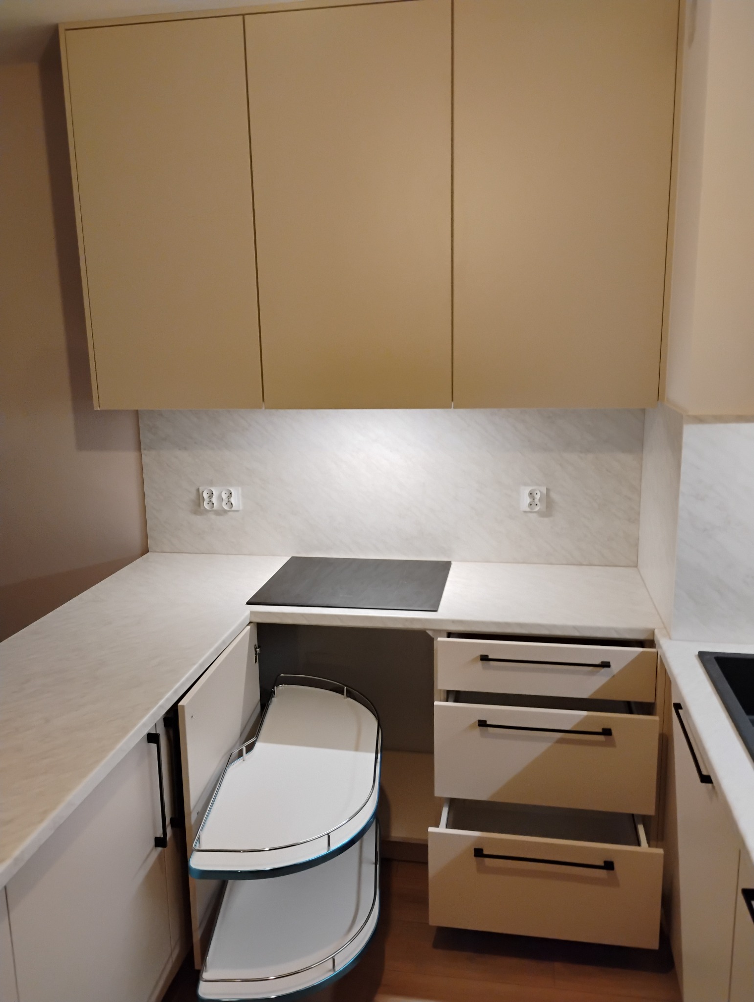 Jasna zabudowa kuchenna z otwartymi szufladami i narożną szafką z półkami obrotowymi, płyta indukcyjna w blacie, minimalistyczne uchwyty.