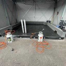 BE- Dach (VELOS) Emil Szukiełowicz - Montaż izolacji bitumicznej na dachu garażu blaszanego, widoczne butle z gazem i palnik dekarski.