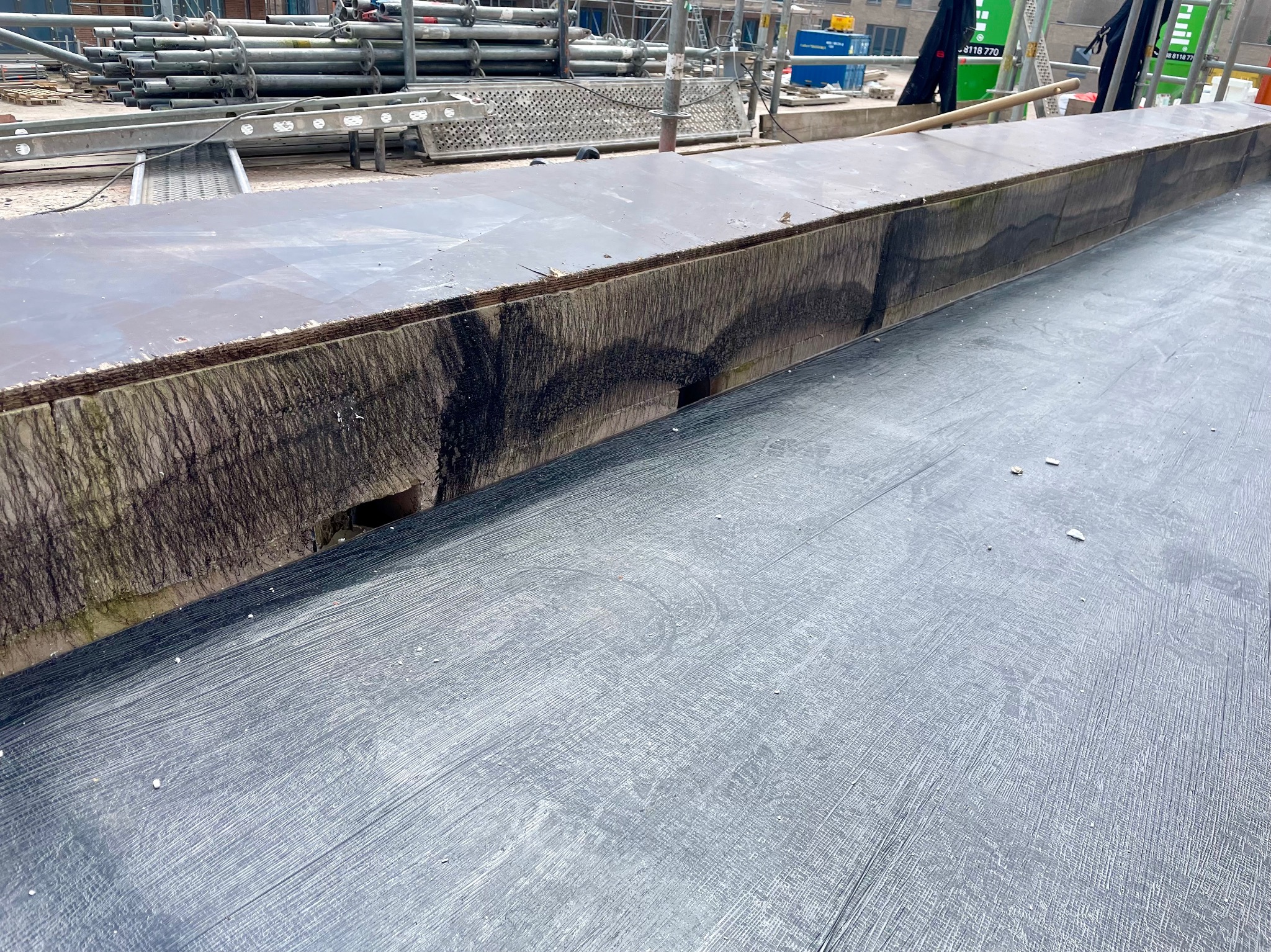 Fragment dachu z widocznymi śladami po wodzie i zabrudzeniami, na tle rusztowania i fragmentu budynku.