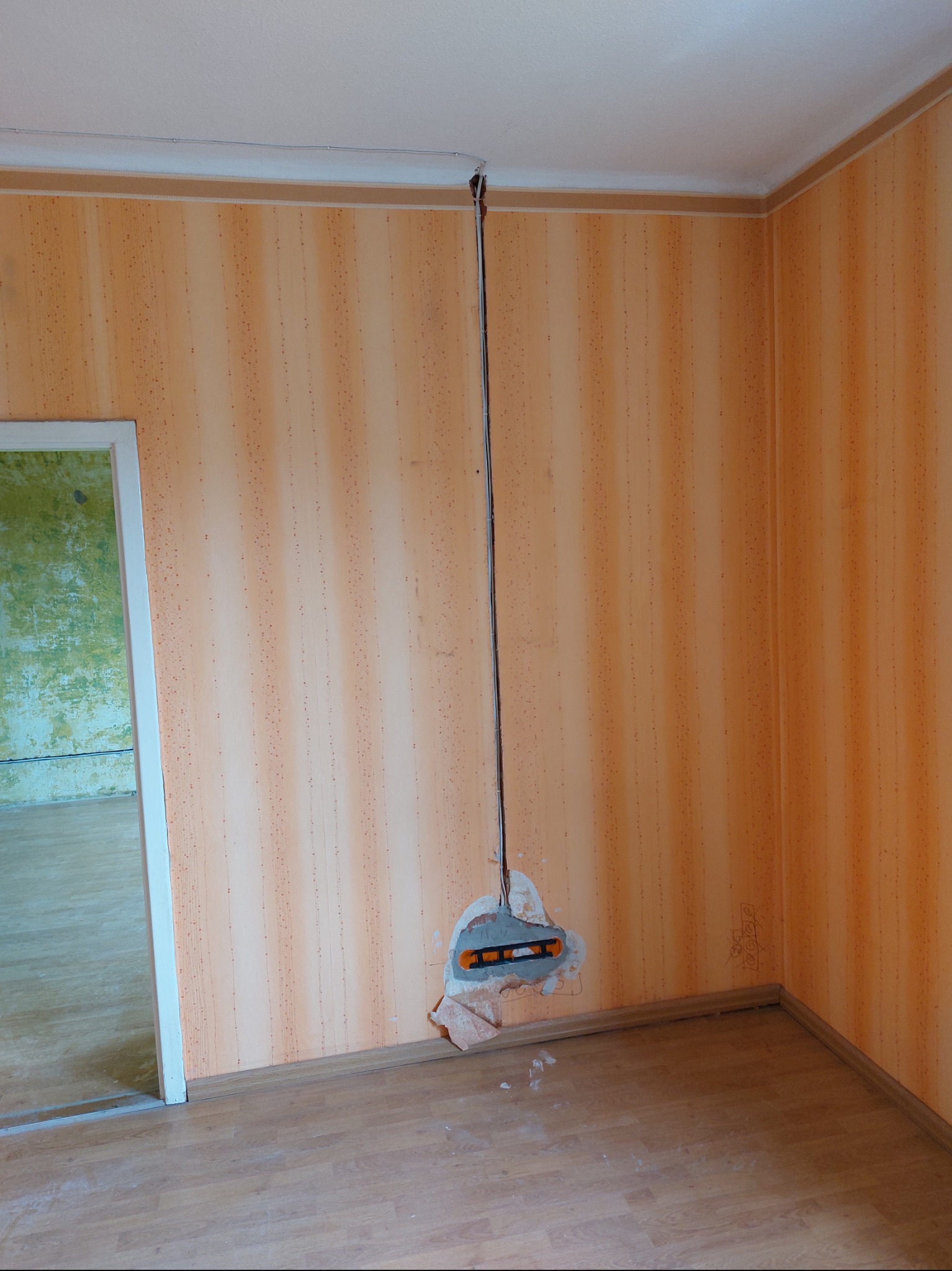 Fragment ściany z odkrytą instalacją elektryczną, widoczna poziomica przy przewodach, pomarańczowa tapeta w tle.