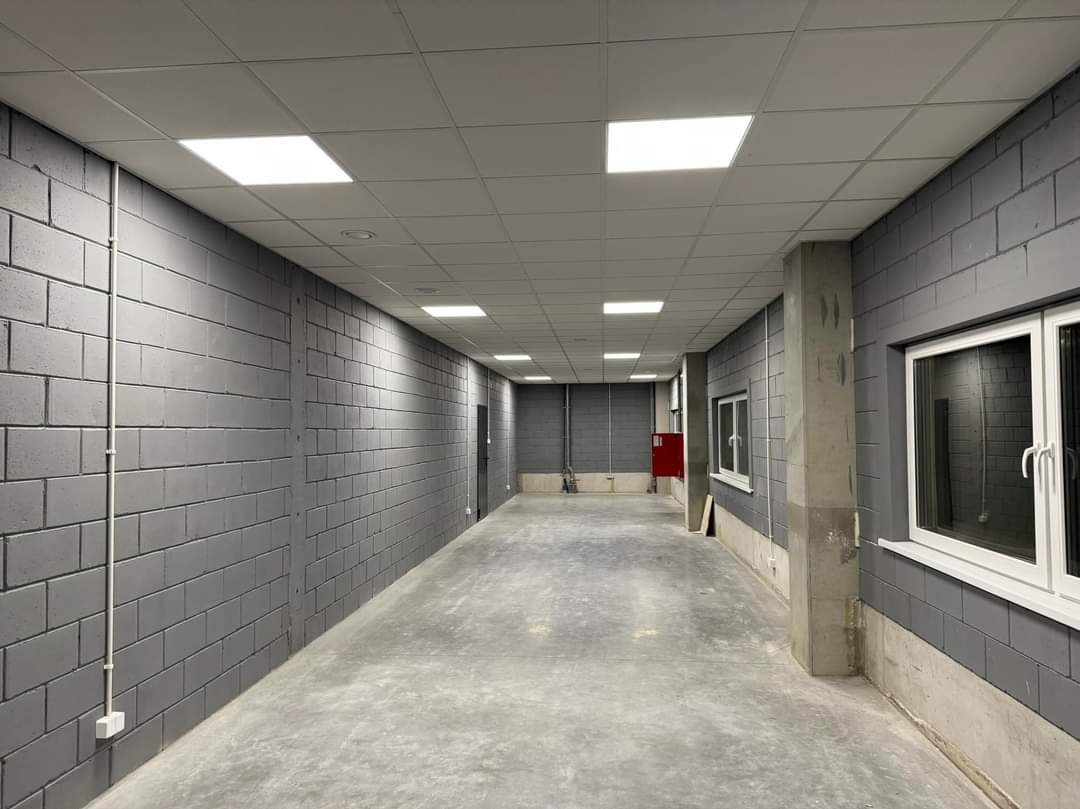 Wnętrze hali z szarymi ścianami z bloczków, betonową podłogą i białym sufitem podwieszanym z kwadratowymi panelami LED.